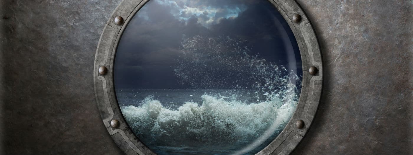 Una vista di onde oceaniche agitate e di un cielo nuvoloso, visti attraverso un oblò metallico rotondo di una nave.