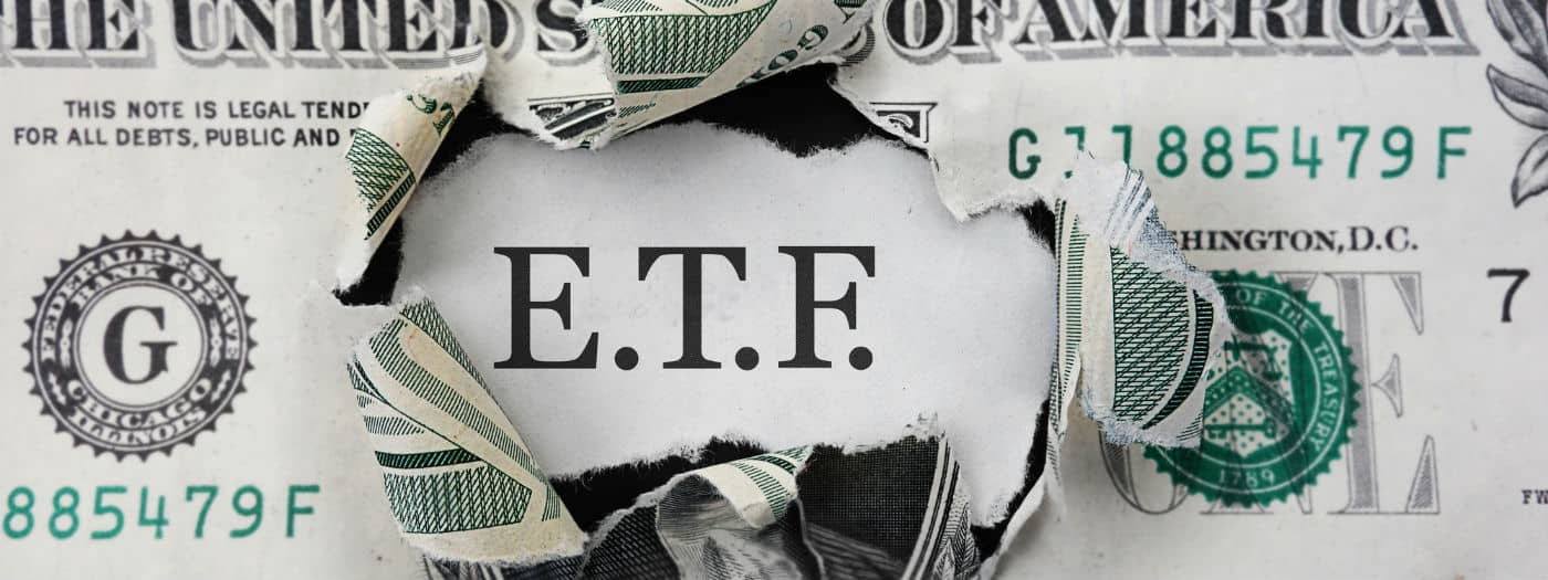 Una banconota da un dollaro statunitense strappata rivela le lettere "ETF" in grassetto, a simboleggiare l'investimento in fondi negoziati in borsa. I bordi strappati incorniciano l'acronimo sullo sfondo della valuta.