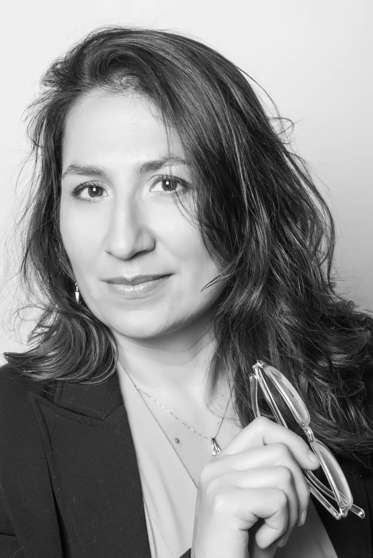 Donna con capelli scuri, giacca scura, tiene occhiali in mano.