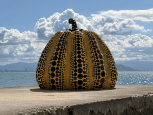 Zucca gialla a pois neri su molo di cemento, con mare e cielo nuvoloso sullo sfondo.
