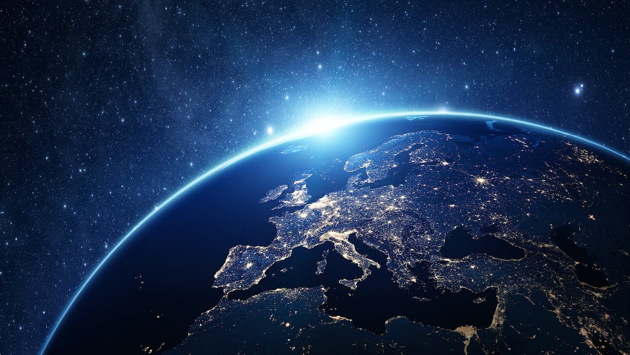 Vista della Terra dallo spazio che mostra l'Europa con le luci della città illuminate di notte. L'orizzonte è illuminato dal bagliore del sole e un cielo stellato fa da sfondo.