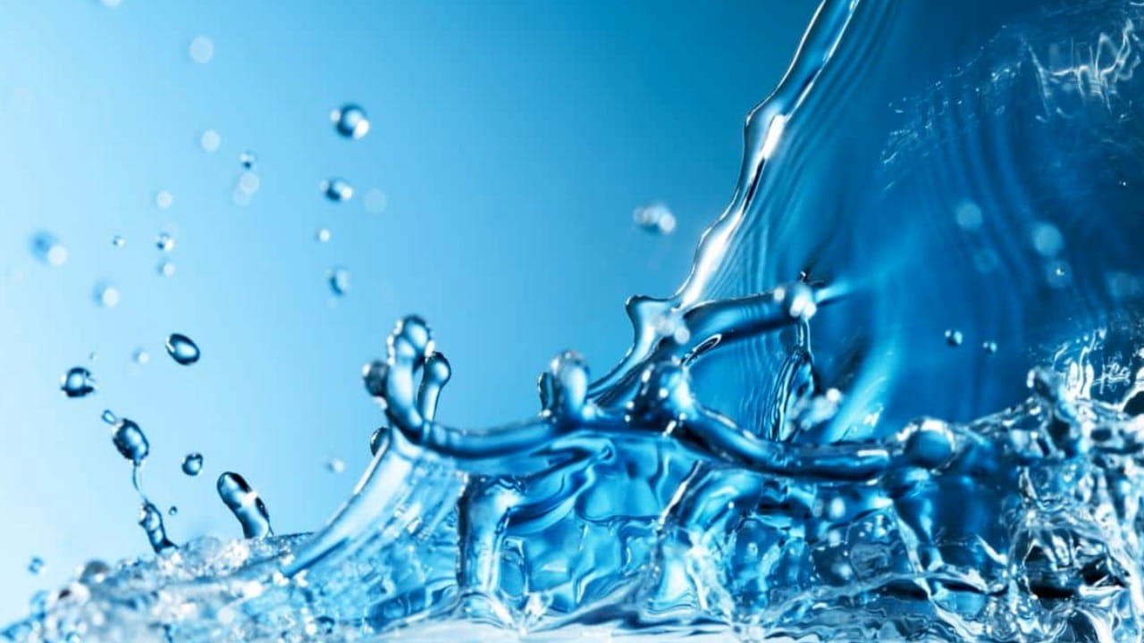 Primo piano di spruzzi d'acqua su uno sfondo blu, che catturano goccioline e onde a mezz'aria. L'immagine trasmette un senso di movimento e freschezza con la luce che si riflette sulla superficie del liquido.