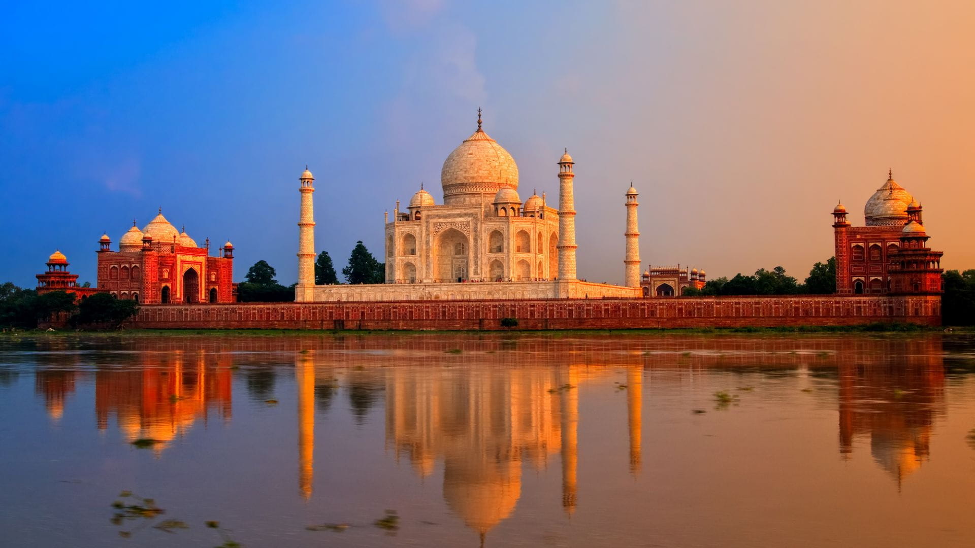 Il Taj Mahal al tramonto, che si riflette nelle acque calme del fiume Yamuna. Il cielo passa dal blu all'arancione, esaltando il marmo bianco del mausoleo e i suoi edifici adiacenti in arenaria rossa.