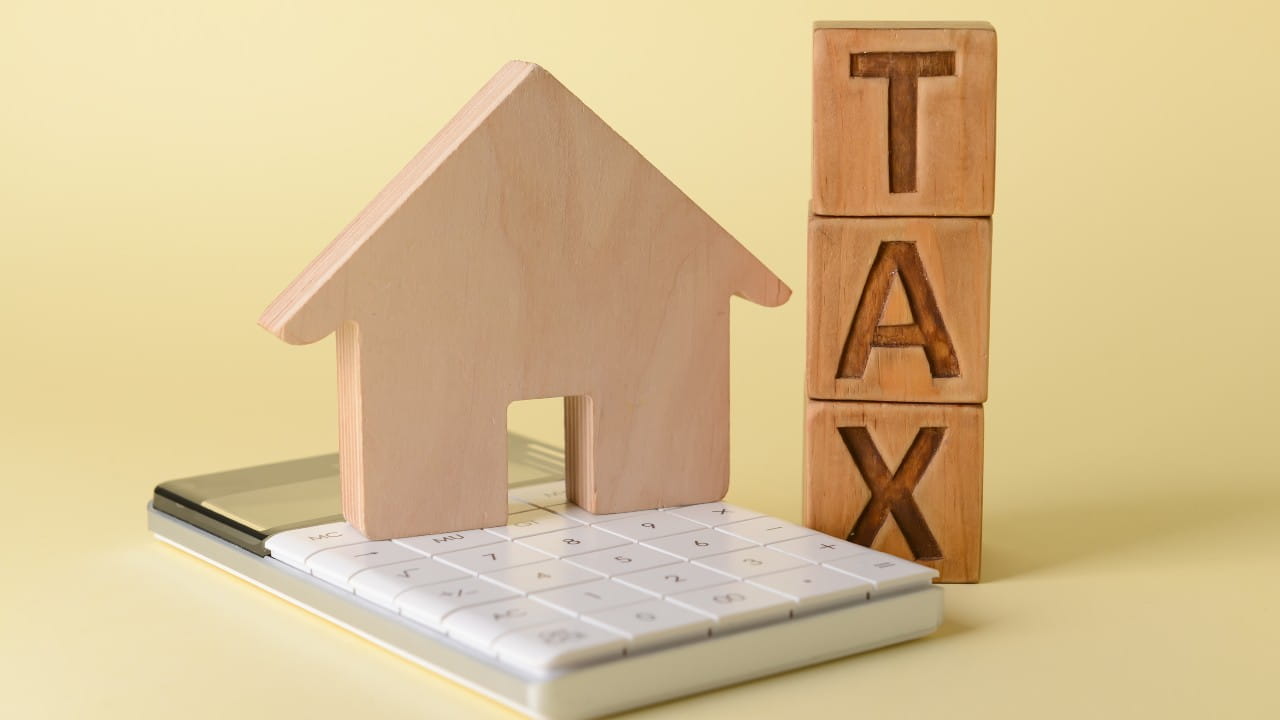 Una figura di casa in legno si trova su una calcolatrice, accanto a blocchi di legno impilati verticalmente che scrivono "TAX", illustrando il concetto di pro rata Iva