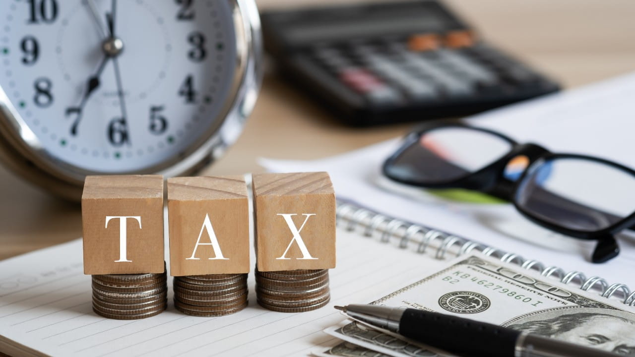 Immagine di una sveglia, la scritta "tax", dei soldi e una calcolatrice. Il riferimento va alla possibilità di costituire una holding di famiglia come strumento chiave per gestire eredità e tasse