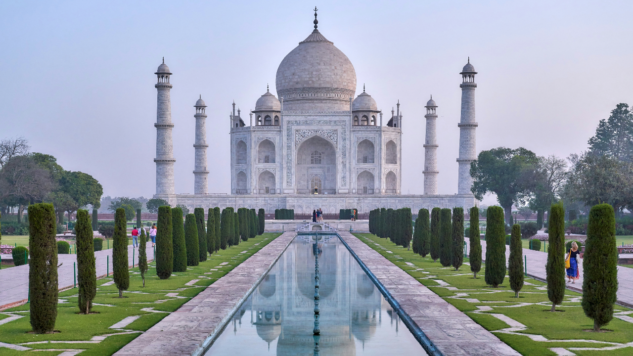 Il Taj Mahal, capolavoro dell'arte mercato indiana, è un mausoleo di marmo bianco con una grande cupola e quattro minareti, che si ergono simmetricamente dietro una piscina riflettente e giardini paesaggistici nelle giornate limpide.