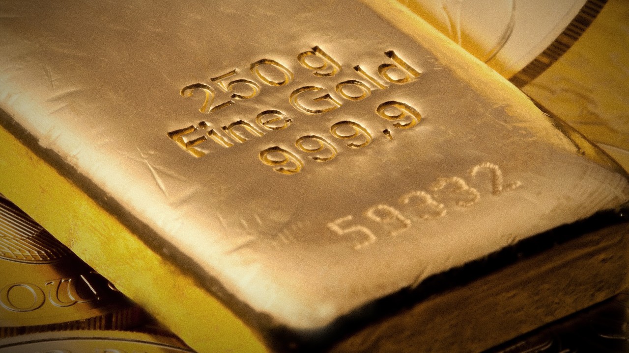 Primo piano di una barra d'oro con la scritta "250 g Oro fino 999,9" e il numero "59332". La barra d'oro poggia su una superficie di monete d'oro lucide e sovrapposte, evidenziandone la consistenza lucida e il colore dorato intenso.