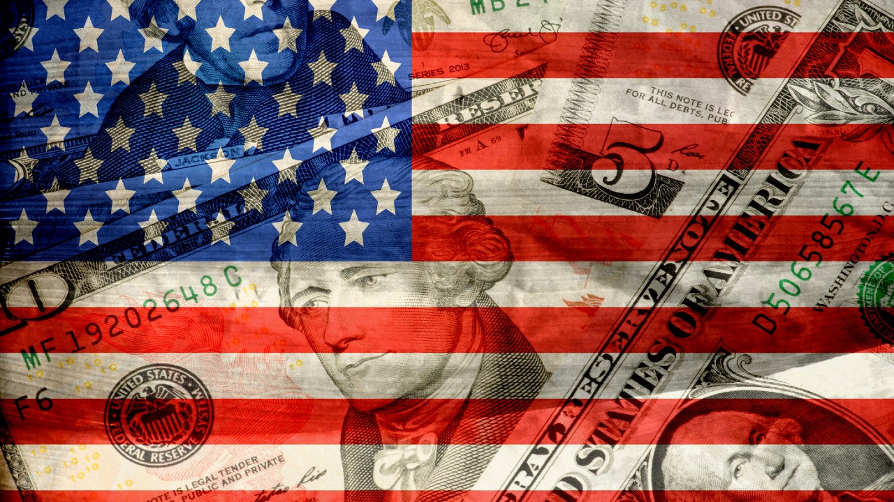 Un collage di una bandiera statunitense sovrapposta a varie banconote da un dollaro statunitense, con ritratti di personaggi storici visibili attraverso le strisce trasparenti rosse e bianche e il campo stellare blu.