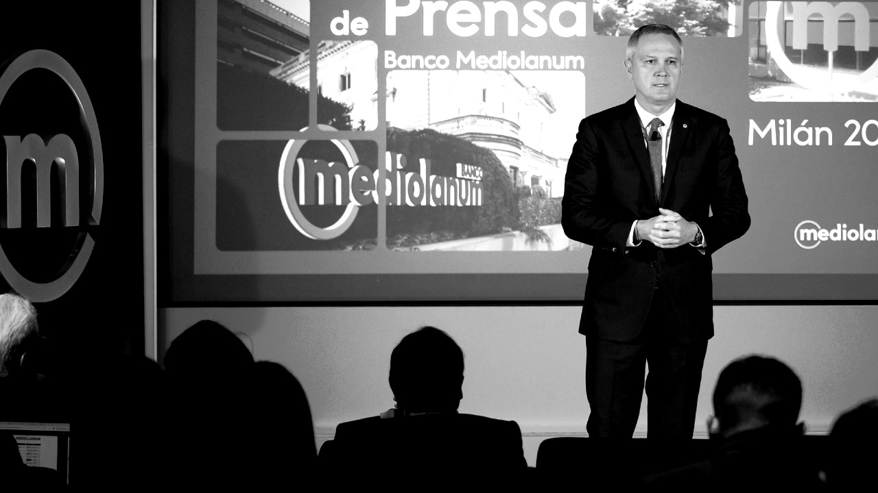 Massimo Doris in giacca e cravatta è in piedi sul palco mentre fa una presentazione di fronte ai giornalisti italiani e spagnoli