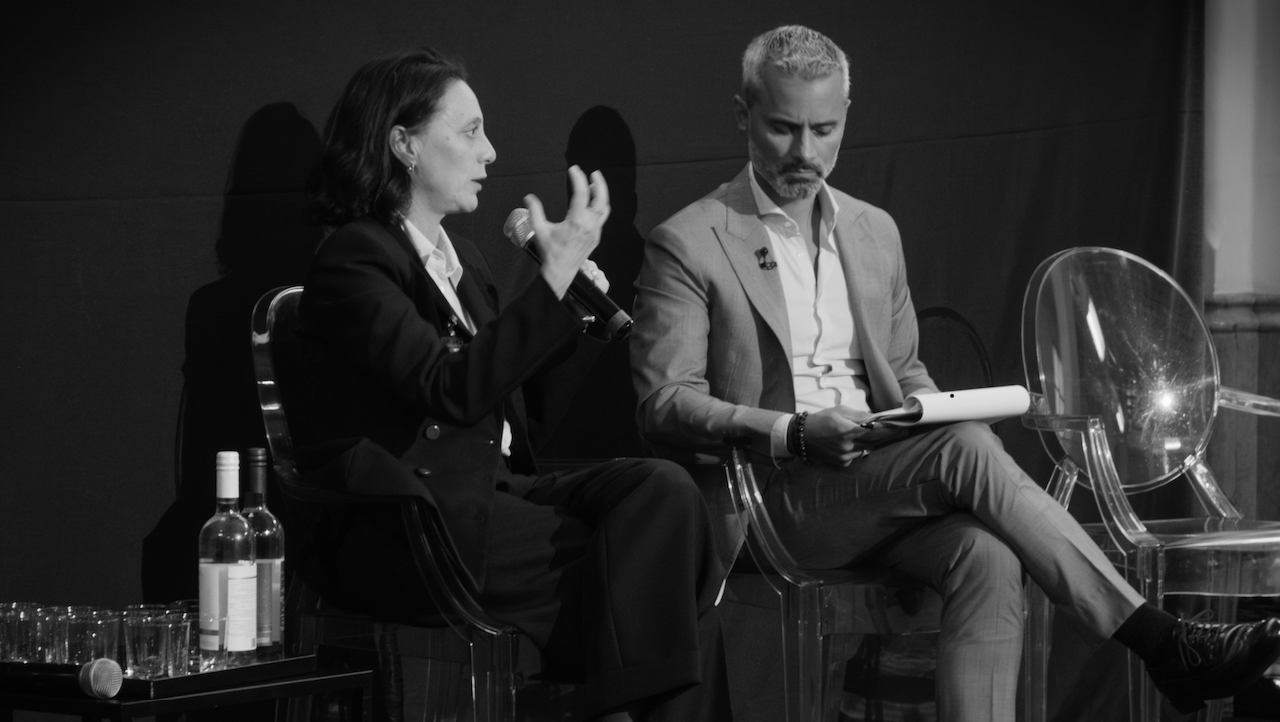 Roberta Gastaldello e Pieremilio Gadda sono seduti sul palco dell'evento Wealth Management Summit di We Wealth, impegnate in una discussione. Il gestore patrimoniale sulla sinistra parla in un microfono, mentre la persona sulla destra tiene in mano un blocco note. Una bottiglia e dei bicchieri sono sul tavolo lì vicino. La scena è in bianco e nero.