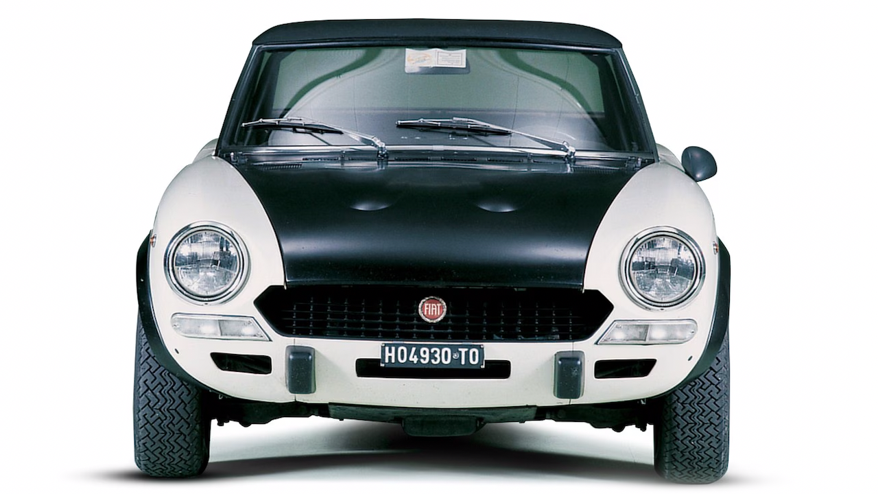 Vista frontale di una classica Fiat con cofano nero e carrozzeria bianca. Il veicolo ha fari anteriori rotondi, un emblema Fiat sulla griglia e una targa con la scritta "HO4930TO". L'auto sembra essere un modello d'epoca, presentata su uno sfondo semplice.
