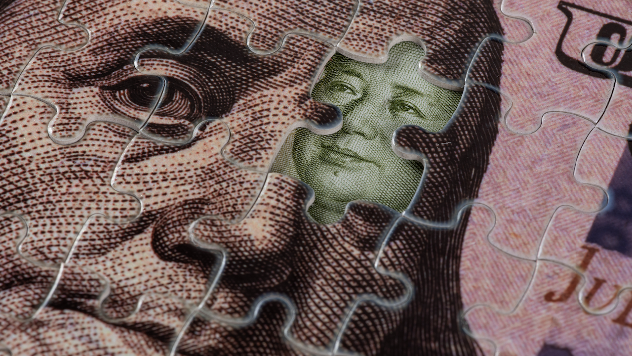 Primo piano di un puzzle con pezzi che mostrano un'immagine dettagliata di Benjamin Franklin dalla banconota da cento dollari degli Stati Uniti. È inserito un pezzo verde di una valuta diversa, che mostra un volto parziale di una persona non identificata.