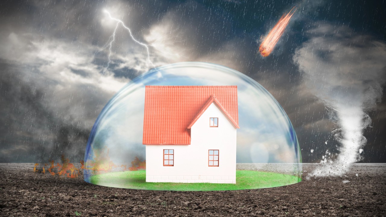 Una piccola casa è protetta da una cupola trasparente in mezzo a una scena caotica con un tornado, fulmini, fuoco, pioggia battente e una meteora nel cielo, a simboleggiare la protezione contro i disastri naturali per l'articolo su "assicurazione casa". assicurazione-casa-mutuo
