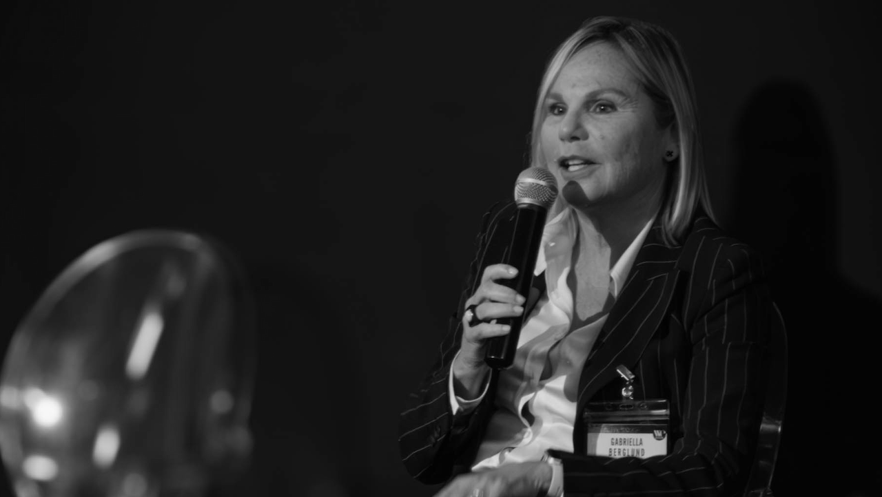 Gabriella Berglund di Comgest, in un tailleur gessato parla al microfono durante una tavola rotonda al Wealth Management Summit. Ha i capelli lunghi e indossa un cartellino con il nome. Lo sfondo è scuro, il che enfatizza la sua presenza.
