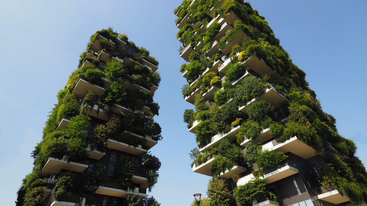 Il bosco verticale a Milano. Due moderni grattacieli con numerosi balconi, ognuno ricoperto da una rigogliosa vegetazione verde, si stagliano contro un cielo azzurro e terso. Queste torri architettonicamente sorprendenti creano un effetto foresta verticale, rafforzando la reputazione della città come una delle città più attrattive.