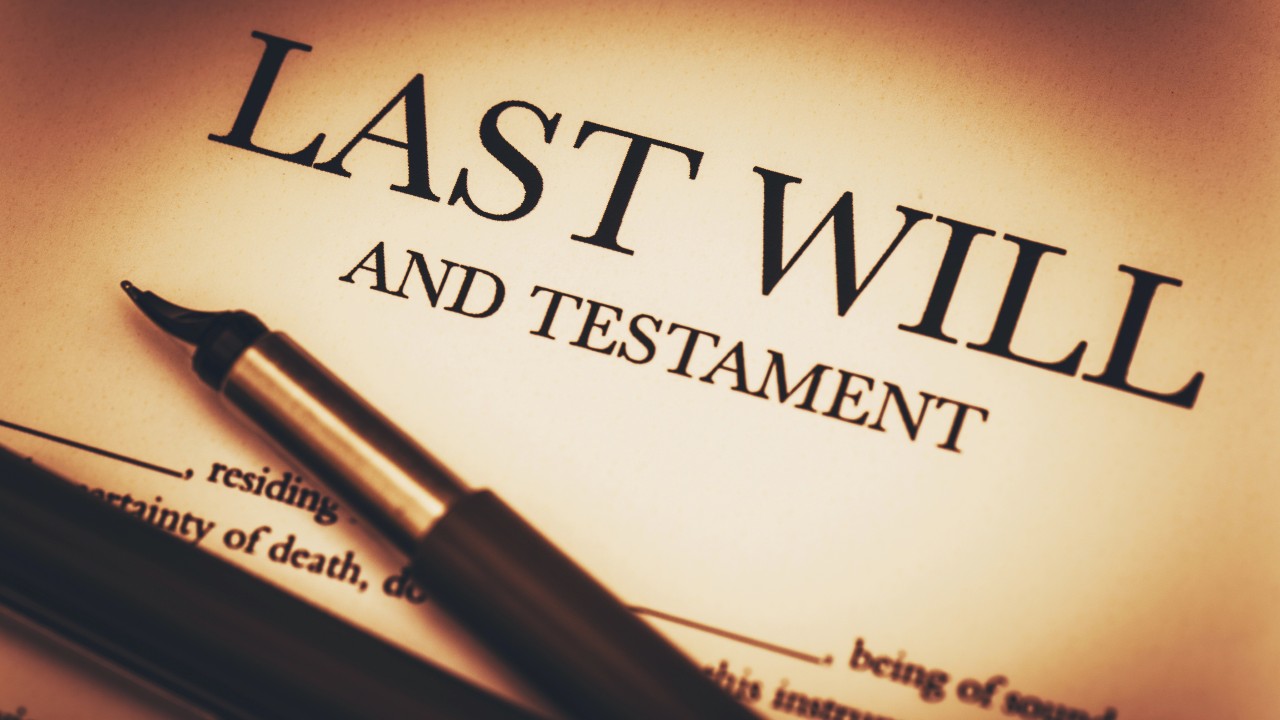 Primo piano di un documento intitolato "Ultime volontà e testamento" con una penna stilografica appoggiata su di esso, a suggerire il processo di stesura o firma di un testamento legale. La calda illuminazione crea un'atmosfera formale e seria.