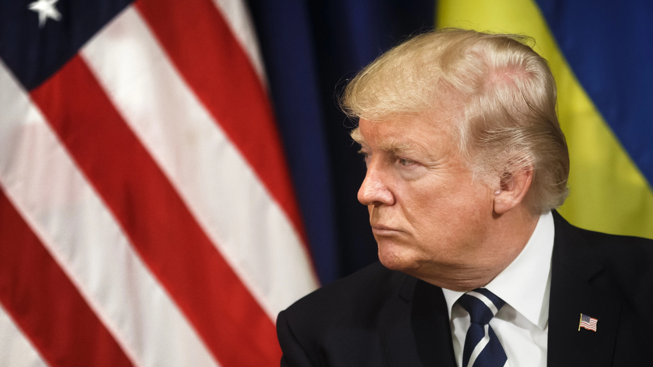 Un uomo biondo in giacca e cravatta guarda di lato, contemplando l'impatto delle azioni europee. Dietro di lui ci sono le bandiere americana e ucraina.