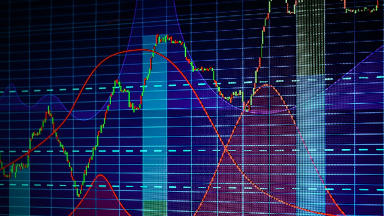 Questa immagine mostra un grafico finanziario colorato con grafici fluttuanti e linee di griglia. Lo sfondo è blu scuro e il grafico presenta varie linee curve in rosso, verde e viola, che indicano diverse tendenze dei dati nel tempo. Il grafico sta a rappresentare l'andamento del mercato del credito.
