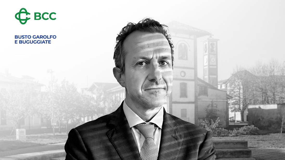 Un uomo in giacca e cravatta è in primo piano con un'espressione seria, incarnando i principi dell'educazione finanziaria. Lo sfondo presenta un'immagine in scala di grigi di un edificio con alberi, mentre il logo della BCC e "Busto Garolfo e Buguggiate" sono ben visibili nell'angolo in alto a sinistra.