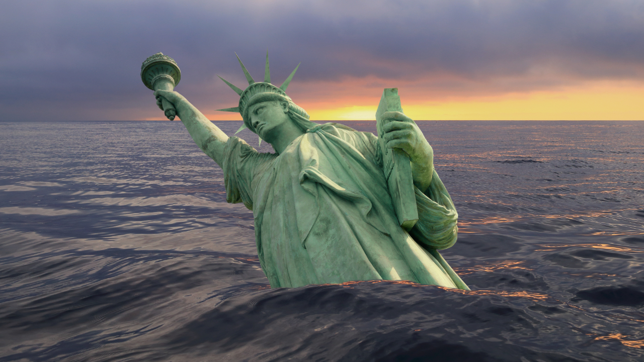 La Statua della Libertà parzialmente sommersa nell'oceano durante un tramonto spettacolare, a simboleggiare l'innalzamento dei livelli del mare. La scena iconica dipinge un quadro potente, molto simile a quello di UBS che affronta le sfide globali. Il sole proietta un caldo chiarore all'orizzonte, in contrasto con l'acqua scura.