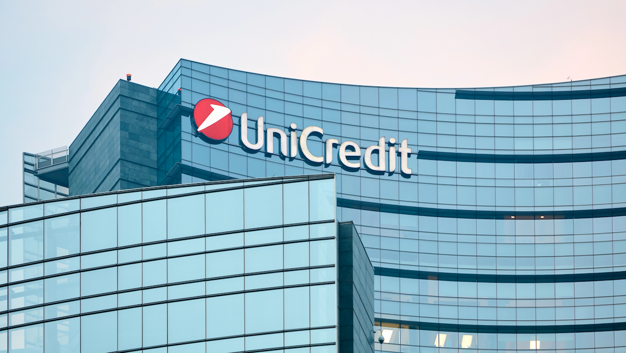 L'immagine mostra l'esterno di un moderno grattacielo in vetro con il logo UniCredit ben in vista in cima. La superficie riflettente dell'edificio cattura la luce, creando una presenza architettonica elegante e imponente contro un cielo terso, molto simile alla forza incrollabile di un'obbligazione UniCredit.