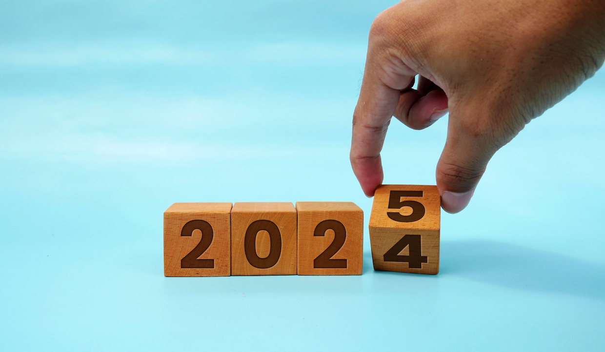 Una mano gira un blocco di legno dal numero 5 al numero 4, formando l'anno 2024 su uno sfondo azzurro.