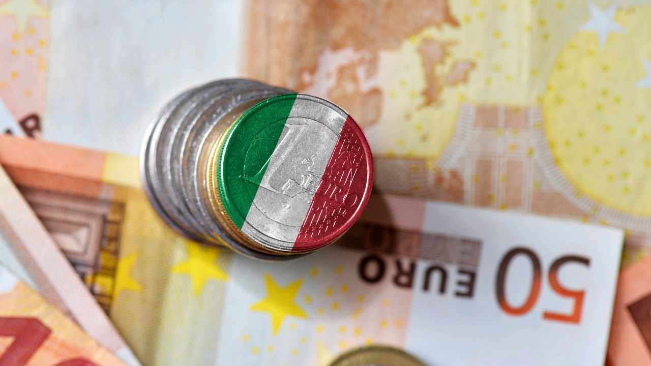Una pila di monete in euro con una bandiera italiana sovrapposta, posizionata sulle banconote in euro.