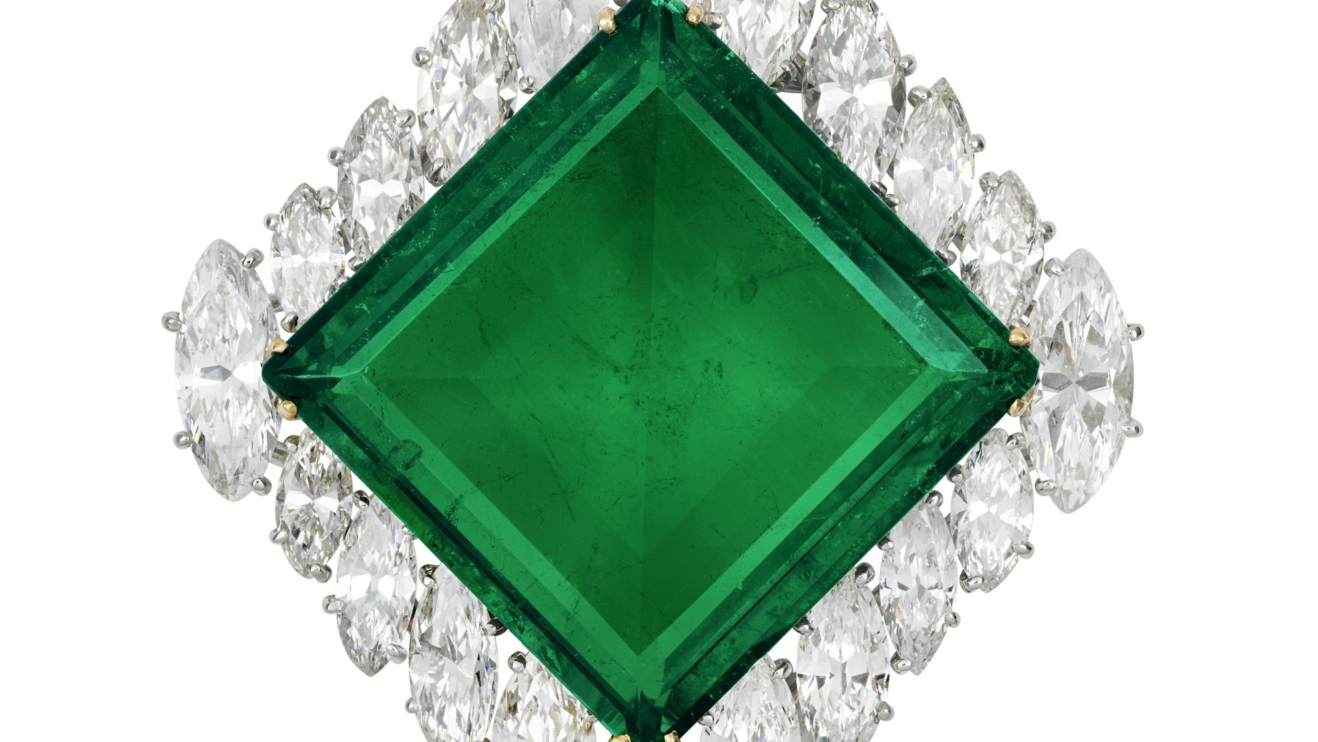 Un grande smeraldo dell'Aga Khan taglio quadrato è incastonato al centro come punto focale, circondato da una disposizione simmetrica di scintillanti diamanti bianchi, creando un design intricato ed elegante.