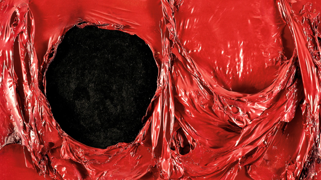 alberto Burri rosso plastica. Primo piano di una superficie rossa, lucida e frastagliata con un grande buco nero irregolare al centro. Il materiale rosso sembra essere allungato e strappato, creando un motivo astratto e strutturato. Il contrasto tra il rosso e il nero è sorprendente.