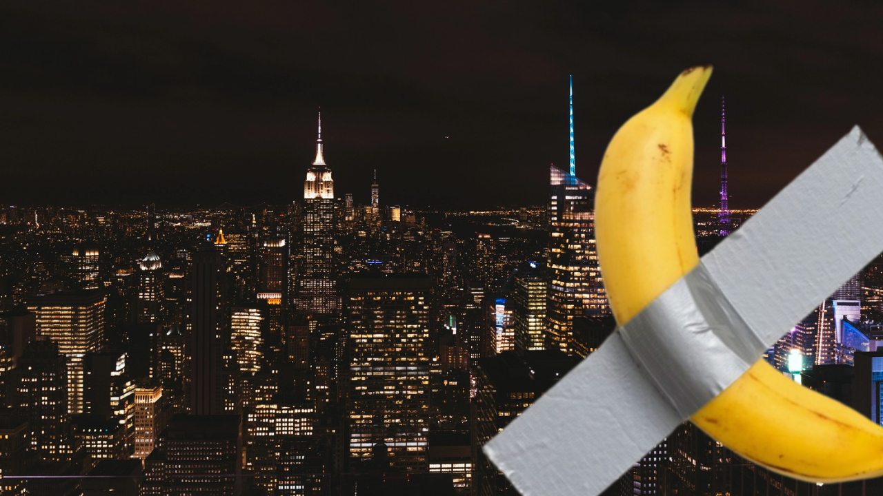 Comedian di Maurizio Cattelan. Una banana, tenuta insieme con del nastro adesivo, è sovrapposta allo skyline notturno di New York City, che mostra alti edifici e luci illuminate.