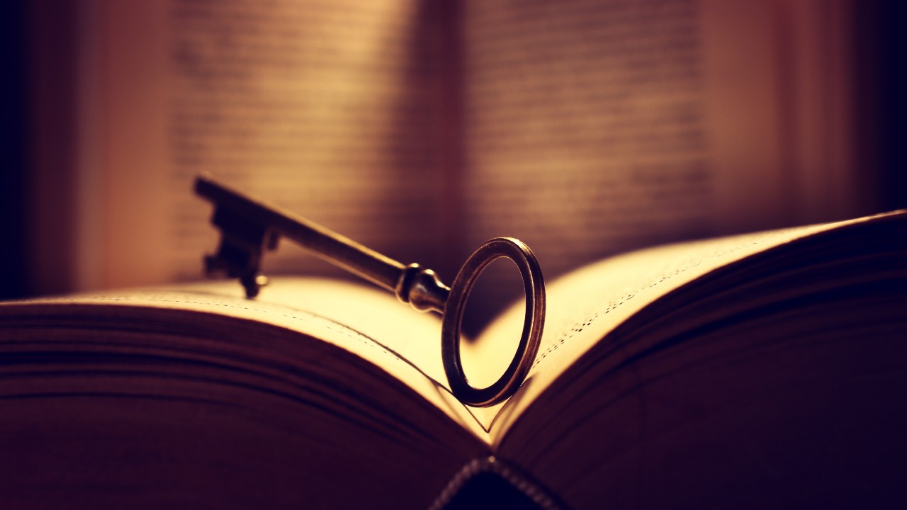 Una chiave d'epoca riposa tra le pagine aperte di un libro, immersa in un caldo chiarore. La luce mette in risalto i dettagli della chiave e del testo. L’immagine viene usata per evocare un certificato successorio europeo da usare nelle successioni transfrontaliere
