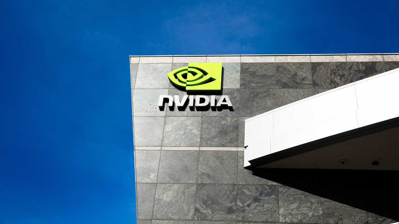 L'immagine cattura l'elegante esterno di un edificio decorato con il logo NVIDIA, il suo emblema verde e le lettere bianche che spiccano su una facciata in pietra grigia, il tutto sotto un limpido cielo azzurro.