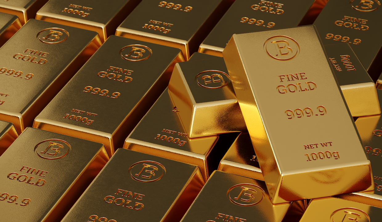 Pile di lingotti d'oro con incisi "FINE GOLD 999.9" e "NET WT 1000g". I lingotti sono disposti ordinatamente, riflettendo una calda tonalità dorata sotto la luce.