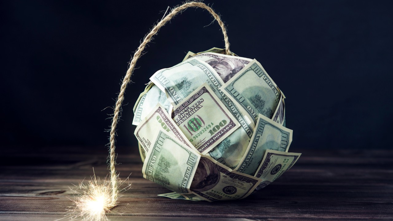 Immagine di una bomba fatta di dollari Usa con una miccia accesa, che evoca la minaccia incombente di una crisi economica, sollevando preoccupazioni sull’introduzione (anche in Italia) di tassa patrimoniale per affrontare tali rischi finanziari.
