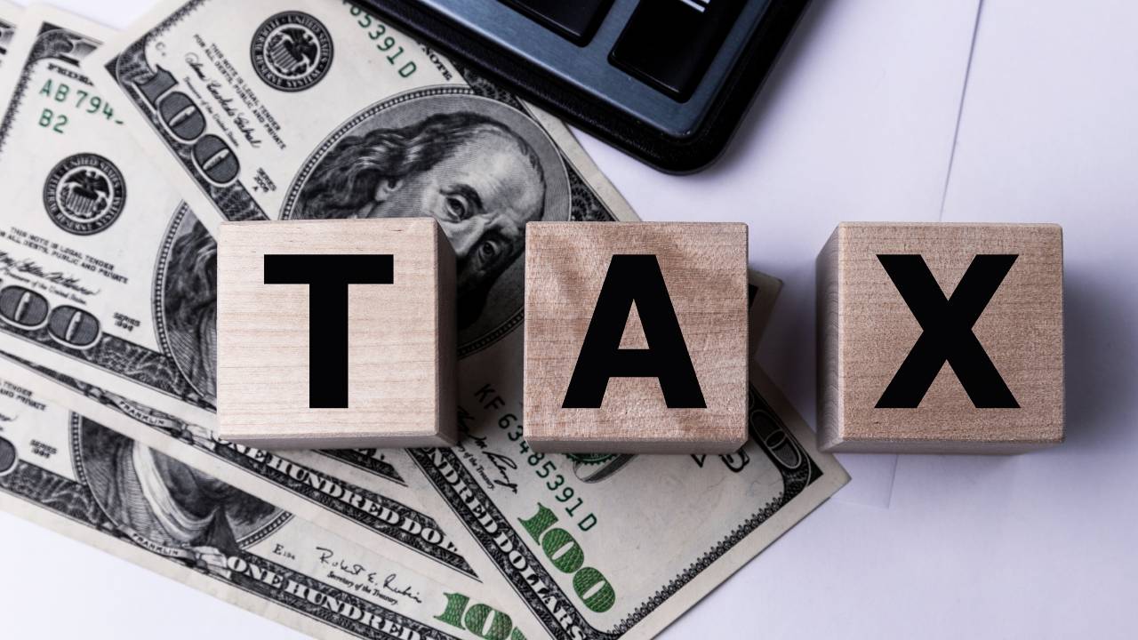 Blocchi di legno con la scritta "Tax" poggiano su alcune banconote da cento dollari statunitensi, a simboleggiare le complessità finanziarie della successione. L'inserimento di una calcolatrice sta a indicare la complessità dei calcoli.