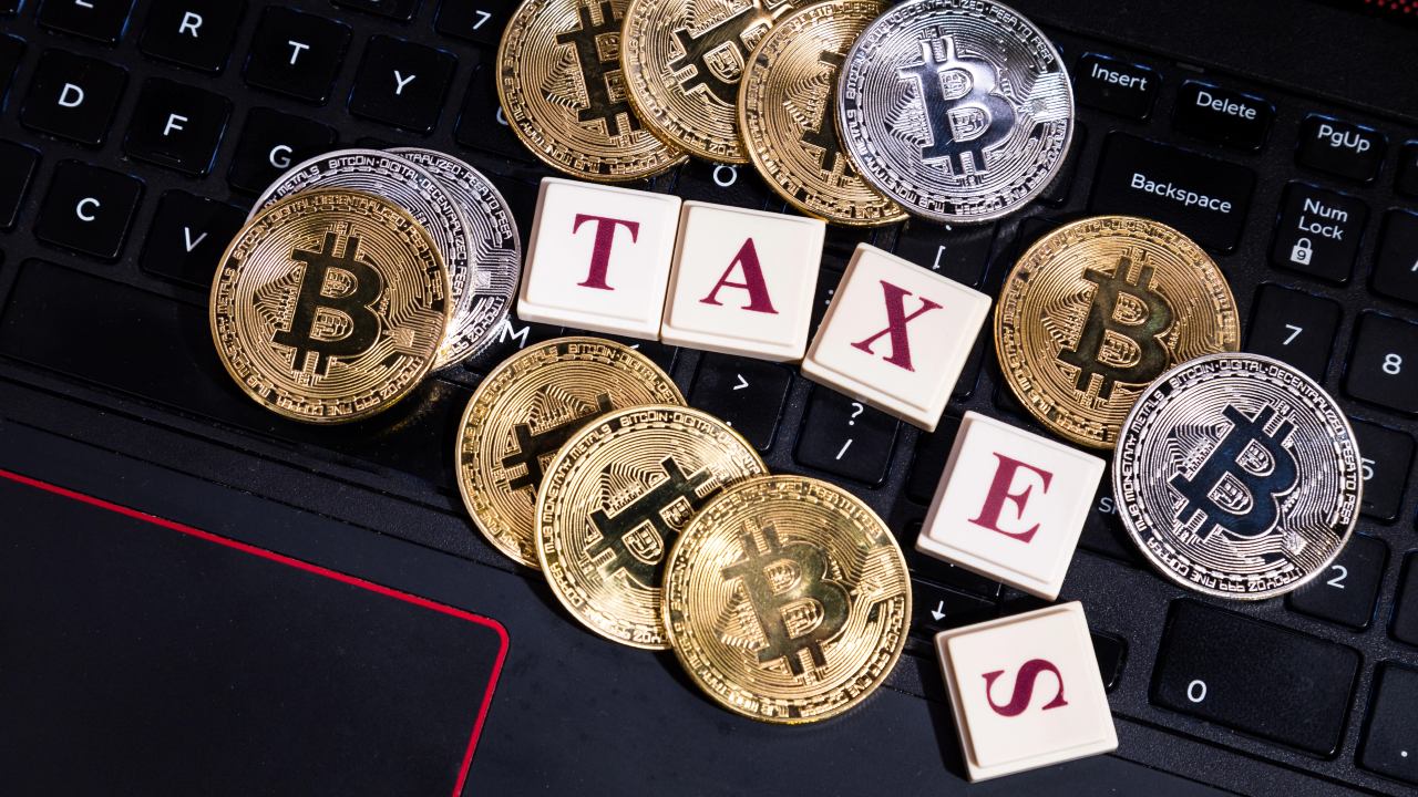 Una raccolta di monete Bitcoin d'oro e d'argento sparse su una tastiera con le lettere che compongono la parola "TASSE" introduce in modo sottile il concetto di tassazione delle criptovalute.