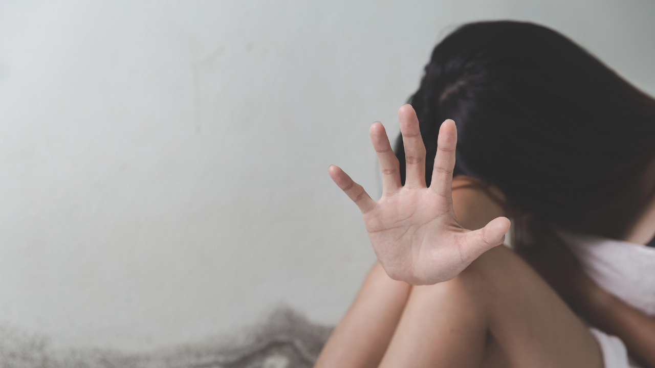 Una donna seduta contro un muro, parzialmente oscurata, tende la mano verso la telecamera in un gesto che la dice lunga contro la violenza. La sua espressione rimane nascosta, sottolineando la sua determinazione a fermare o scongiurare qualcosa di invisibile.