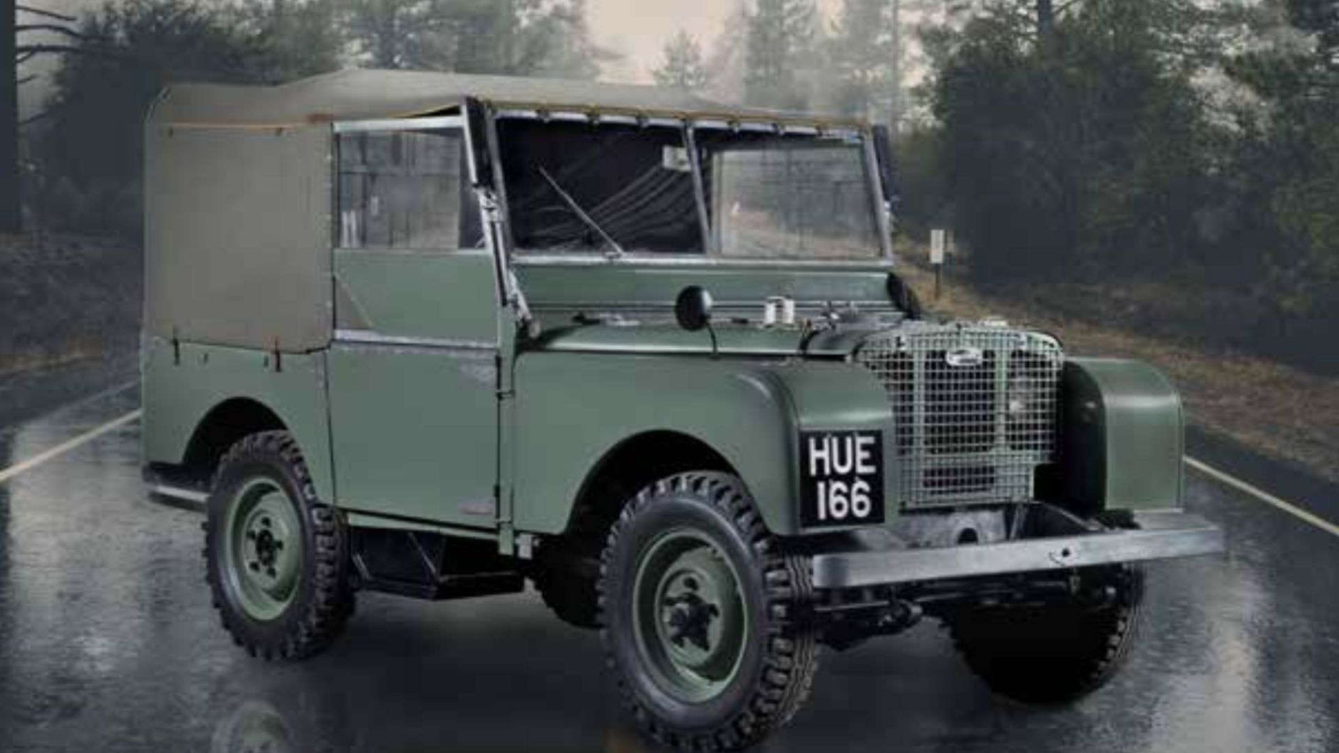 Una Land Rover verde prima classic con capote in tela è parcheggiata su una strada bagnata in mezzo a uno sfondo boschivo. La targa dell'auto recita "HUE 166" e la scena cattura magnificamente una giornata piovosa in campagna.