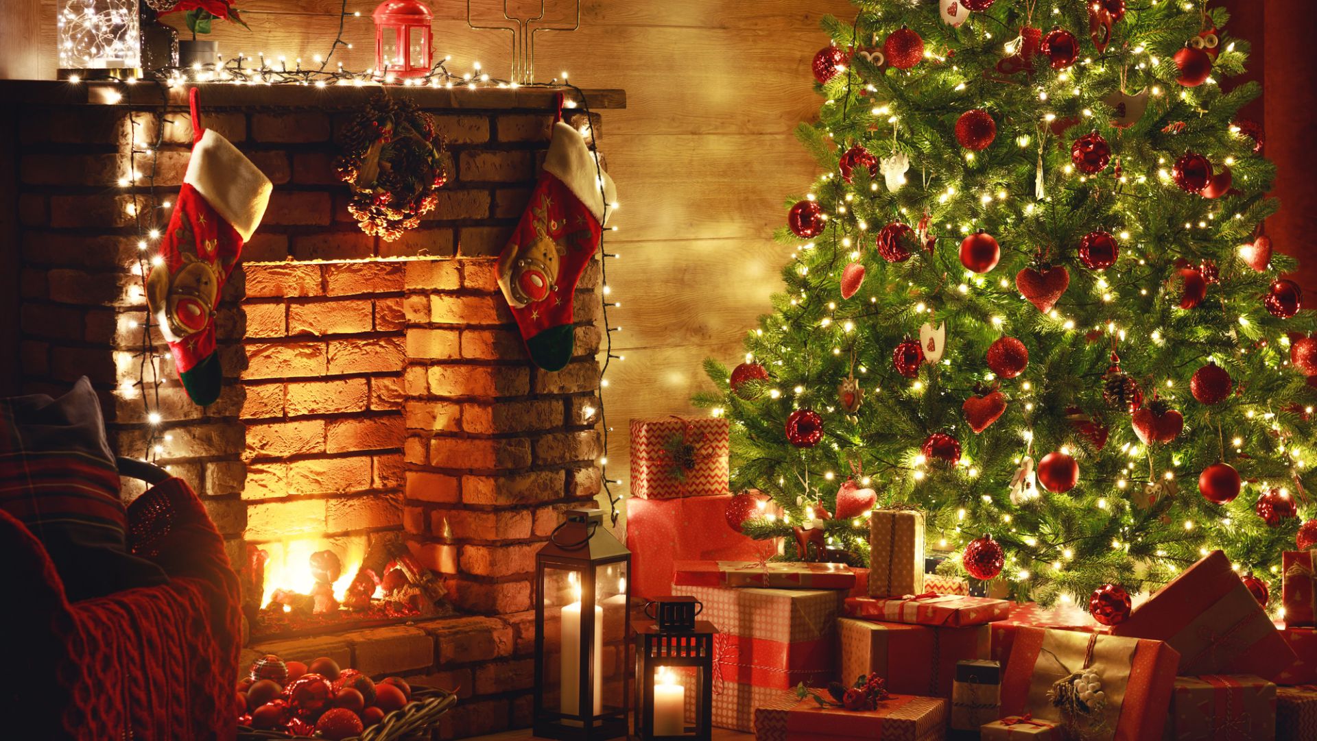 Un accogliente soggiorno con un camino acceso decorato con calze e luci. Un albero di Natale decorato con luci e ornamenti rossi si trova lì vicino, circondato da regali incartati. Il caldo chiarore crea un'atmosfera festosa.