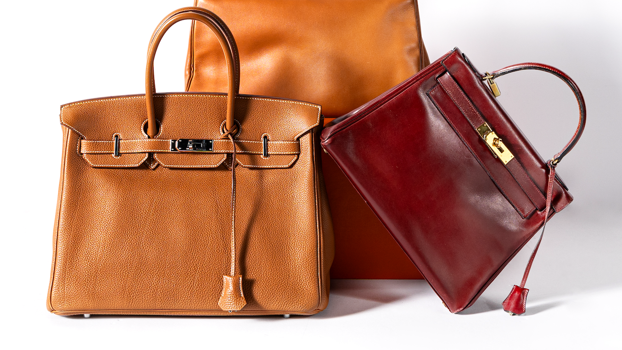 Sono esposte tre borse di lusso: una tote bag in pelle marrone chiaro, una borsa in pelle marrone rossiccio con chiusura in oro e una borsa in pelle testurizzata marrone chiaro con lucchetto. Le borse sono disposte su uno sfondo bianco.
