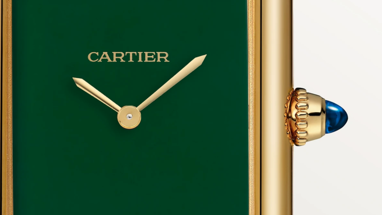 Primo piano di un orologio Cartier con quadrante verde e lancette dorate. Il lato presenta una corona dorata con un cabochon blu. Il design dell'orologio è elegante e minimalista.