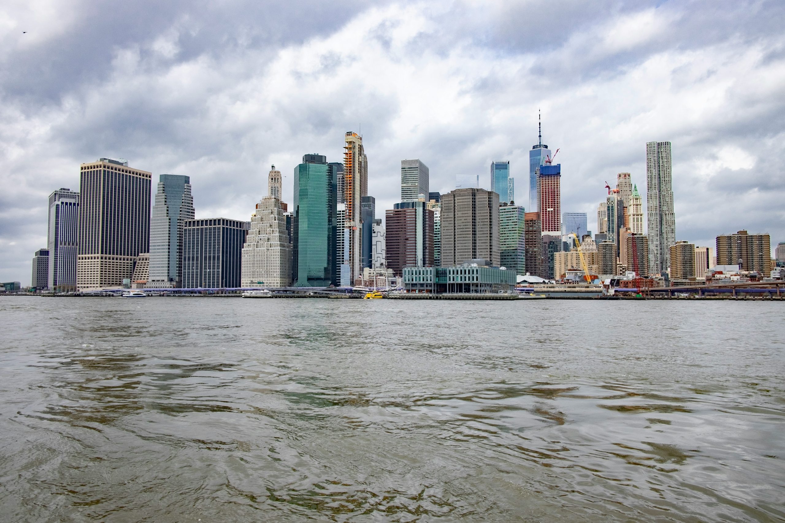 Veduta dello skyline di una città con edifici moderni e tradizionali, sotto un cielo nuvoloso, vista da uno specchio d'acqua.