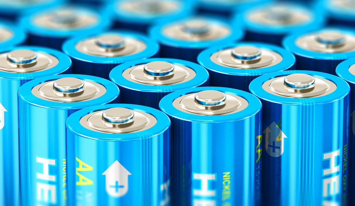Un'immagine ravvicinata di diverse batterie AA blu. Le batterie sono allineate in file, con i terminali positivi rivolti verso l'alto, con una parte superiore argentata ed etichette che indicano la polarità positiva. La superficie è lucida e metallica.