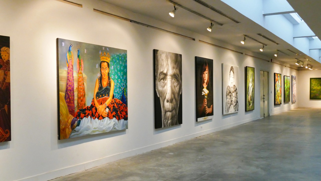 Una galleria d'arte moderna, come espressione di una collezione d'arte di un'impresa familiare, presenta dipinti colorati su una parete bianca immacolata. Le opere d'arte, tra cui ritratti e stili astratti, sono illuminate da luci a binario sopraelevate. Il pavimento liscio in cemento completa il design spazioso e minimalista.
