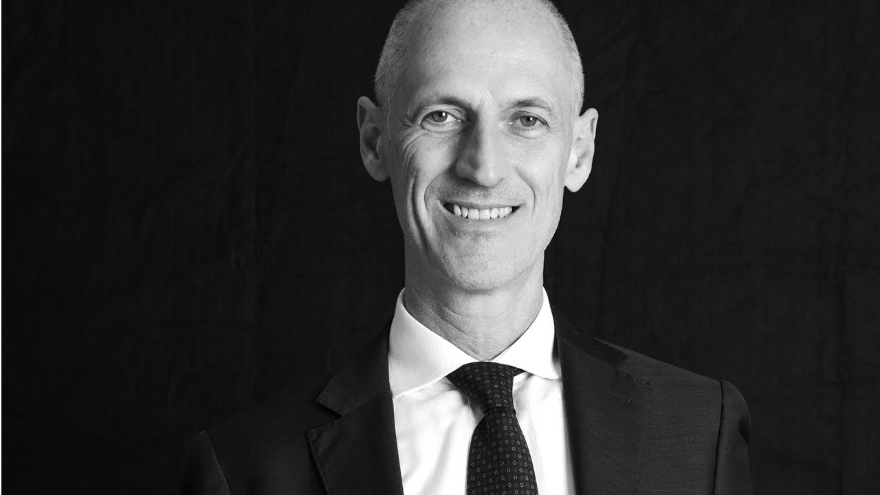 Ritratto in bianco e nero di Luca Bonansea sorridente in giacca e cravatta su uno sfondo scuro, che trasuda l'eleganza tipica di Bnp Paribas Private Banking.