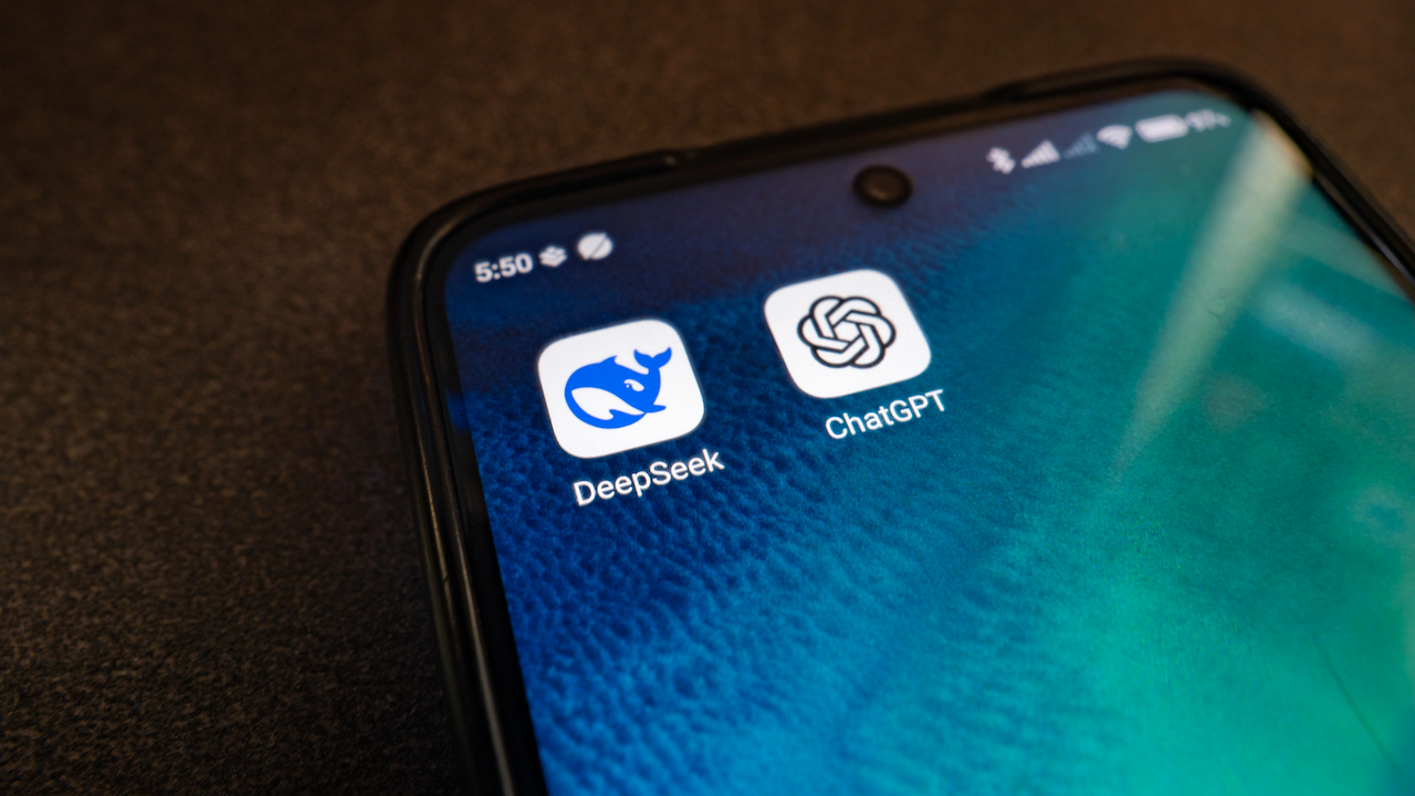 Primo piano dello schermo di uno smartphone che mostra due icone di app: DeepSeek con un simbolo astratto blu e ChatGPT con un motivo a incastro. Lo sfondo è una carta da parati con texture verde-blu.