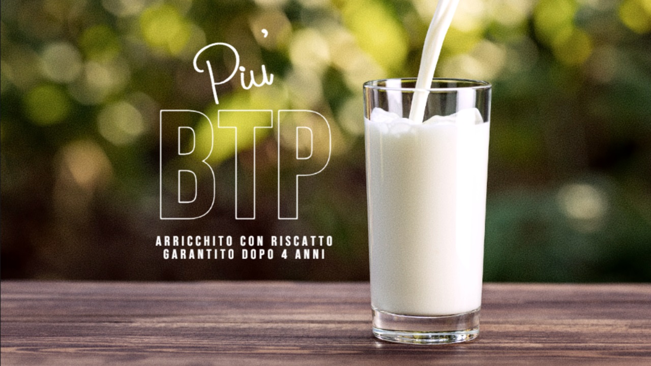 Un bicchiere di latte viene versato su un tavolo di legno con uno sfondo verde sfocato. Il testo recita: “Più BTP, arricchito con riscatto garantito dopo 4 anni”.