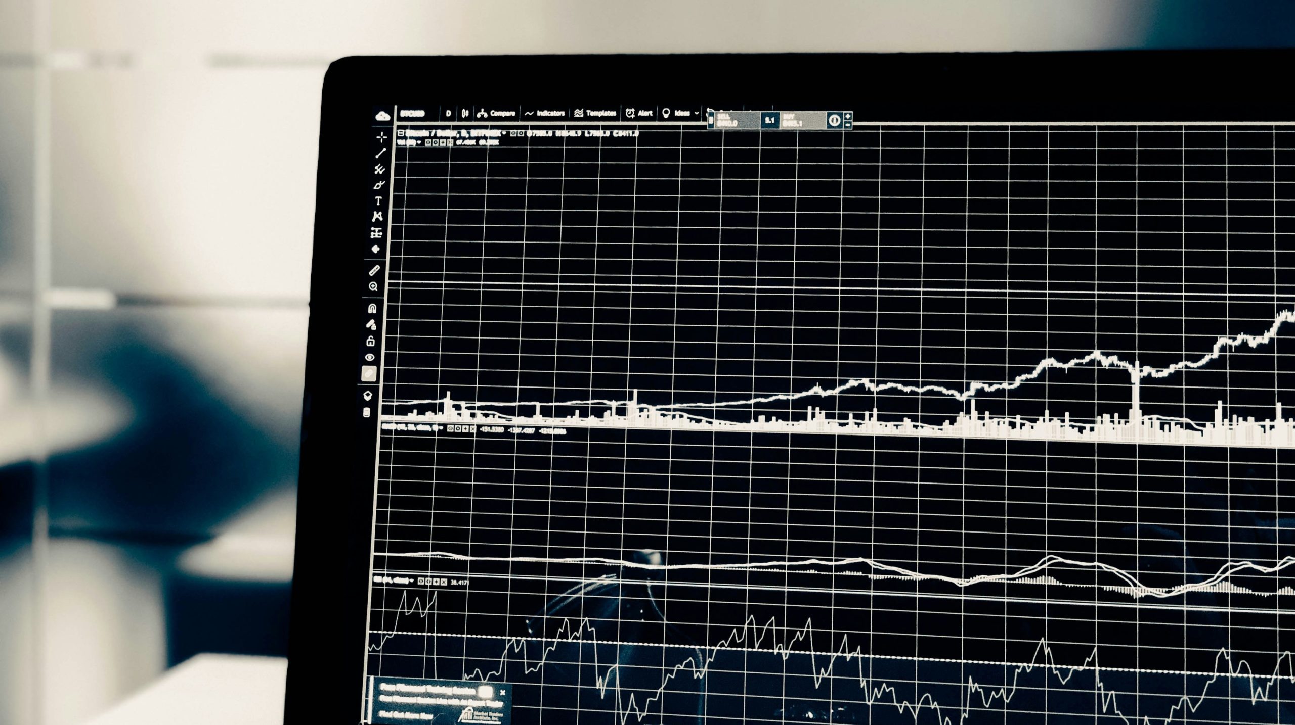 Uno schermo di laptop che mostra un grafico finanziario con linee che rappresentano i dati del mercato azionario. Grafici multipli mostrano tendenze al rialzo e al ribasso su uno sfondo a griglia.