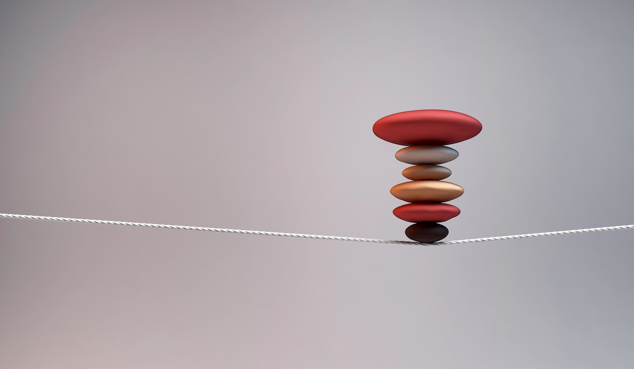 Una pila di pietre colorate e lisce in precario equilibrio su una corda tesa su uno sfondo semplice, illustra il tema dell'equilibrio e della stabilità.