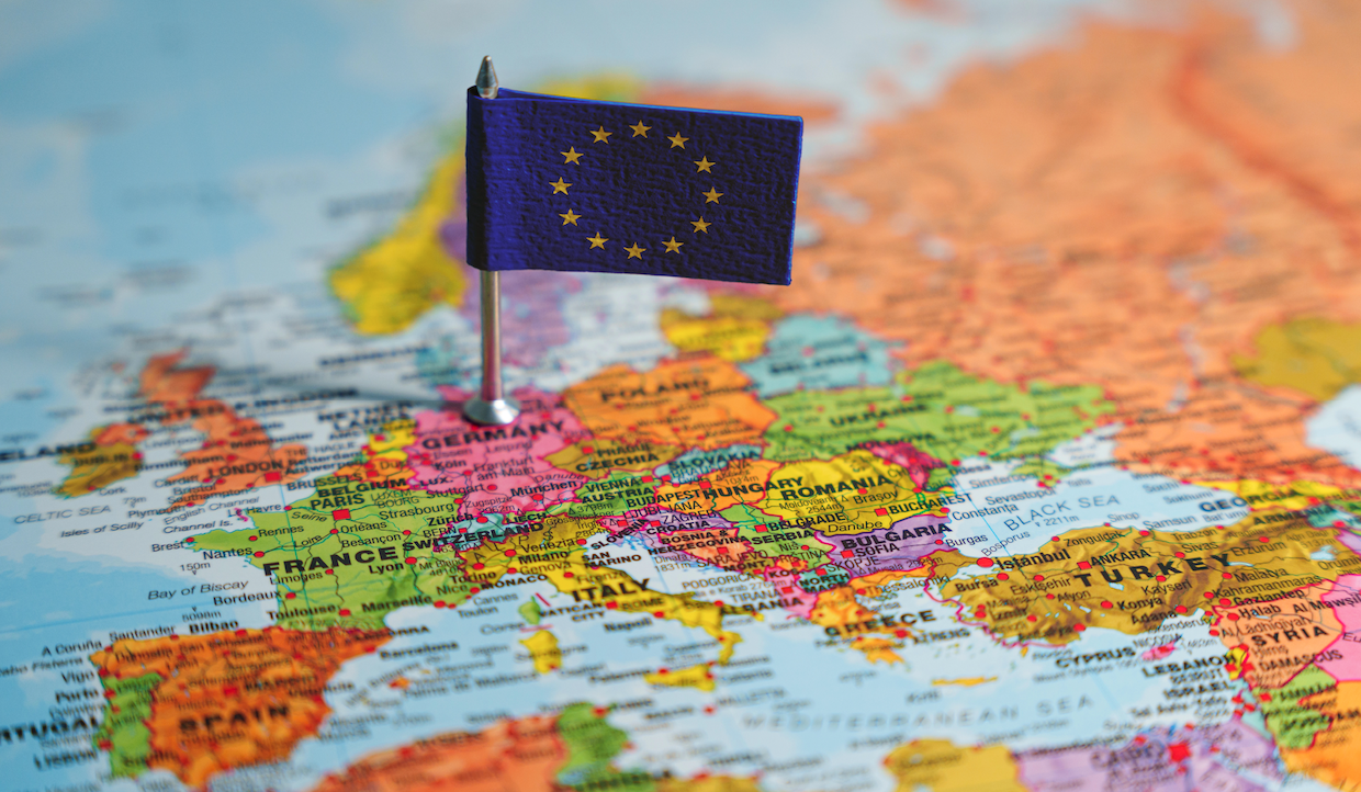 Una piccola bandiera dell'Unione Europea su una puntina è posizionata su una mappa dell'Europa, centrata sulla Germania. La mappa mostra vari paesi tra cui Francia, Italia e Polonia, con confini e nomi chiaramente visibili.